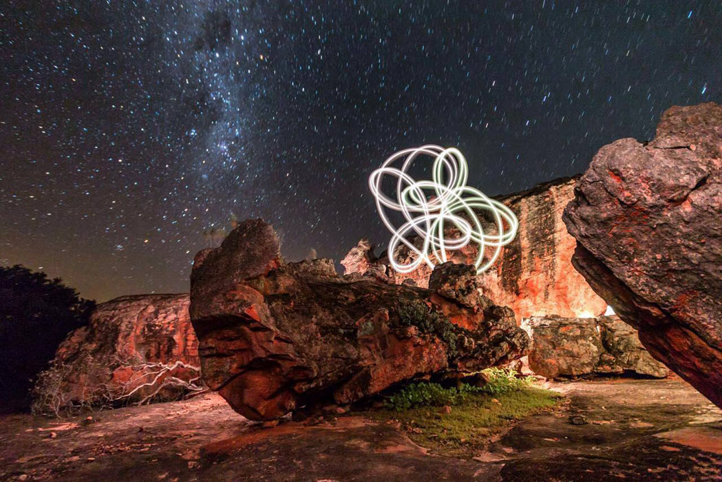 long exposure photo of the night sky in the cederburg with a pod poi making light trails on a boulder